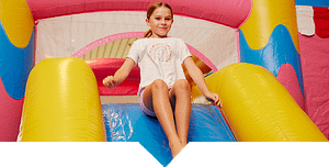A girl sitting at the top of a slide on a jumping castle.