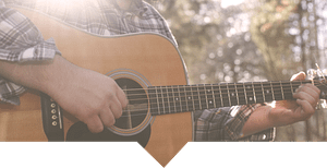 A country music player holding an acoustic guitar in the bush.